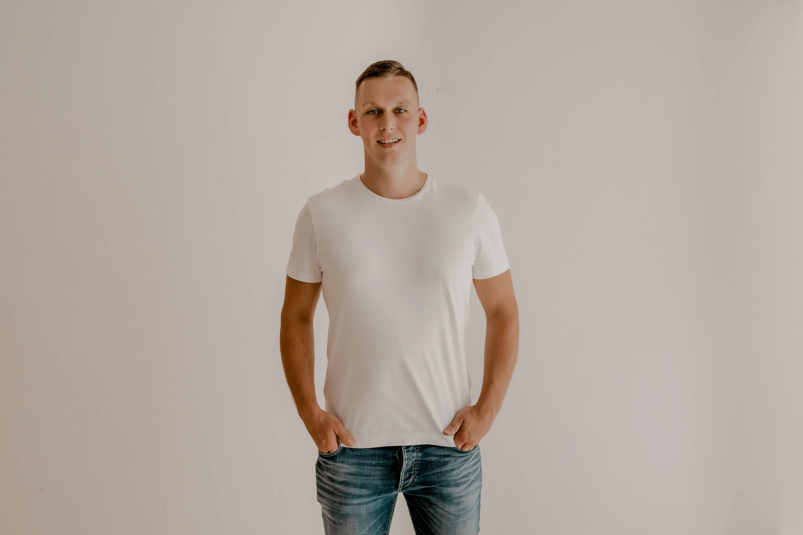 Stefan Bergner, Hochzeitsvideograf in Bautzen, lächelt im weißen T-Shirt und Jeans vor einer hellen Wand.