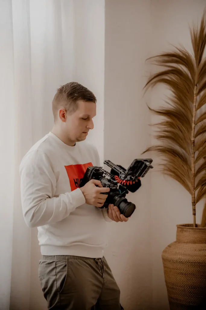 Stefan Bergner, Hochzeitsvideograf in Dresden, hält eine Filmkamera mit Monitor und Mikrofon am Fenster.